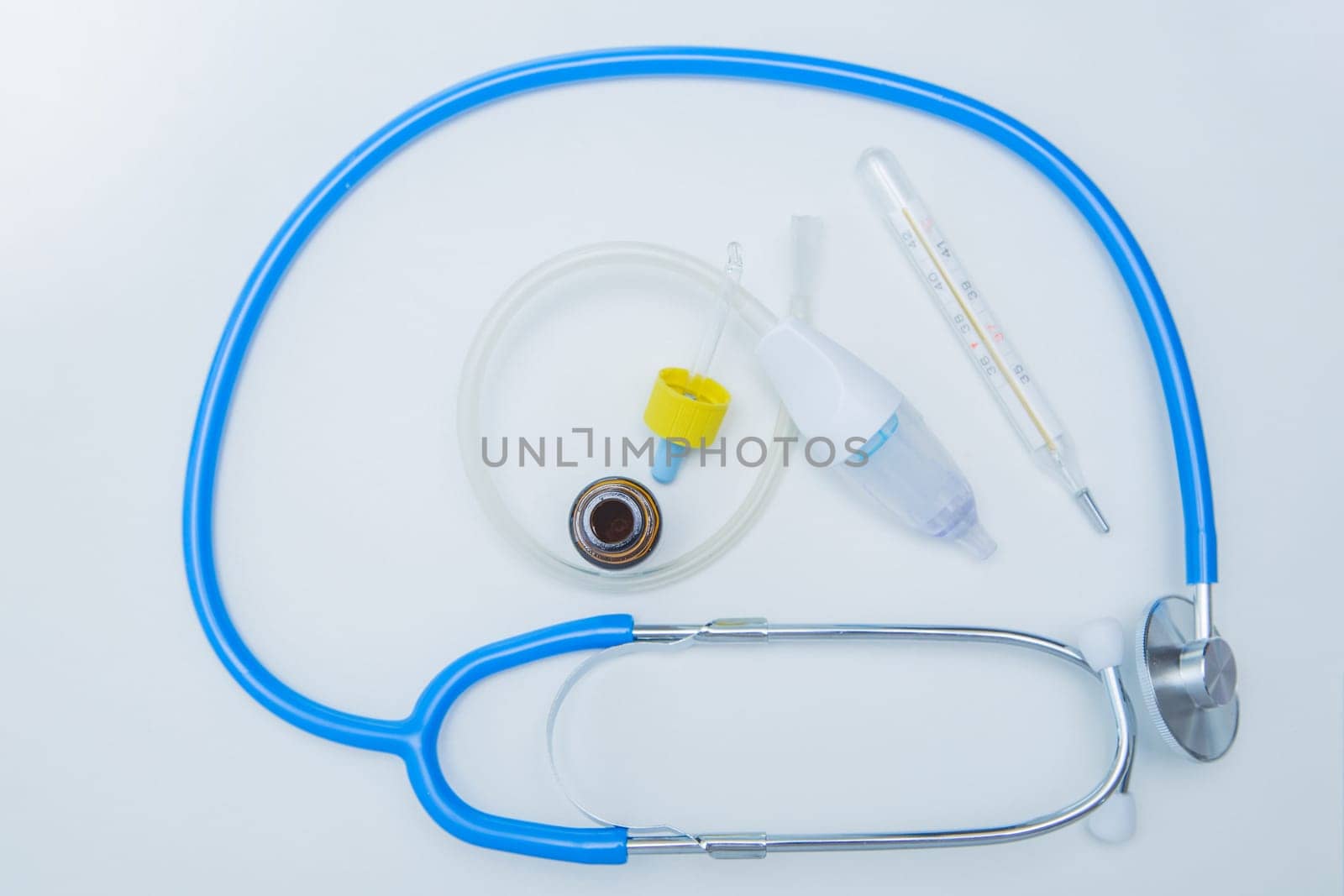 The stethoscope lies on a white background around, inside it is a baby aspirator, nose drops and a thermometer. High quality photo