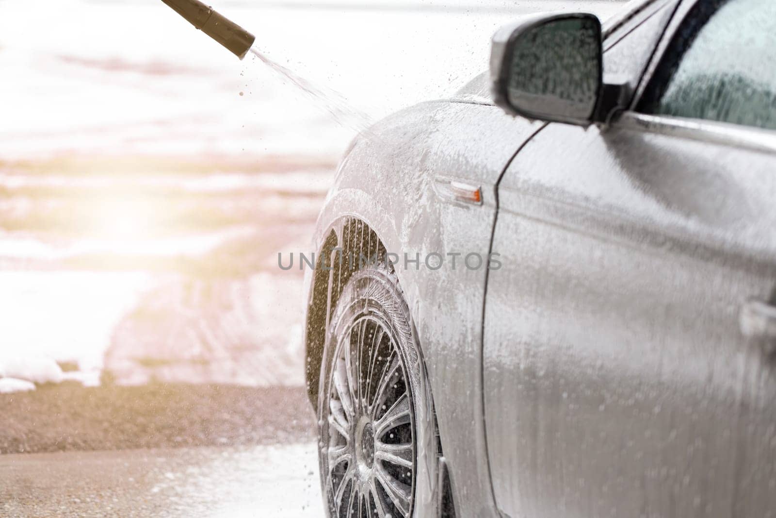 Purifying automobile with touchless technology in exterior carwash. Cleaning car with high pressure on sunlight. Washing vehicle manual with water and soap.