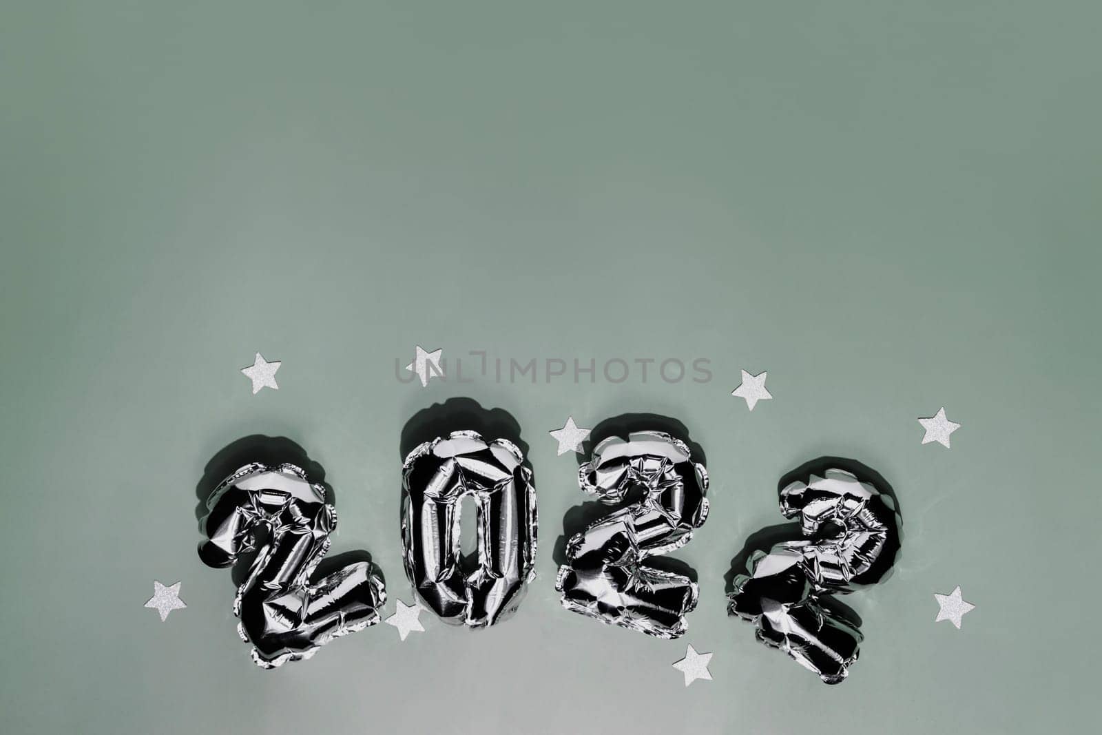 New Year 2022 or Christmas green background flat lay. Top view on 2022 balloon silver or metallic numbers with white star shapes. Invitation or greeting card concept. Festive mood. High quality photo