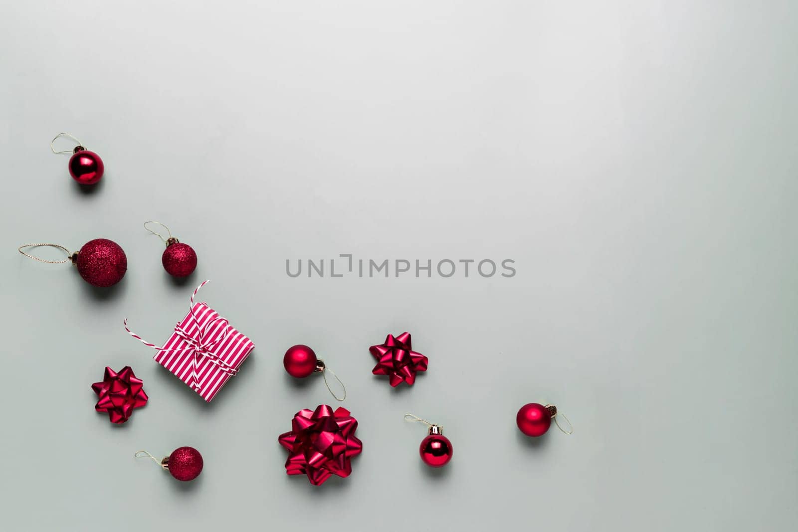 Gray background with pink Christmas gift box present, small red Christmas balls or sphere toys, ribbon bows for fir tree, other decorations. Christmas sales, shopping or greeting card or invitation