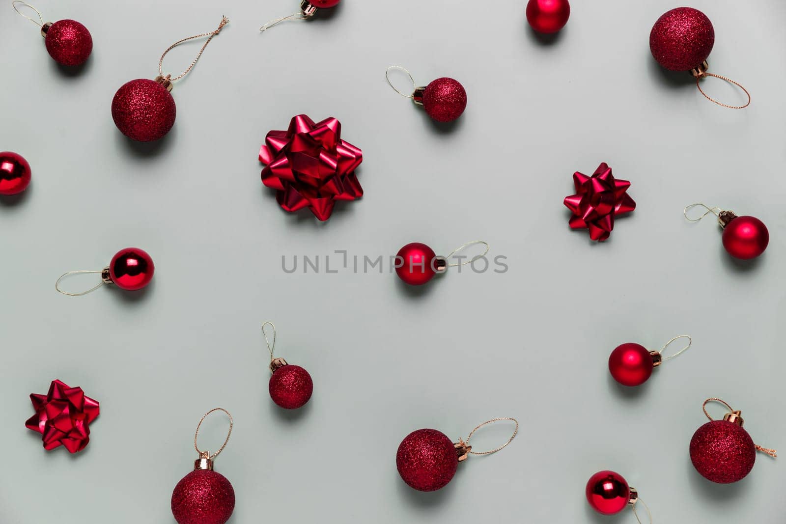 Pattern on gray background with small red Christmas balls or sphere toys, ribbon bows for fir tree. Concept for festive greeting card or invitation for Christmas eve celebration. High quality photo