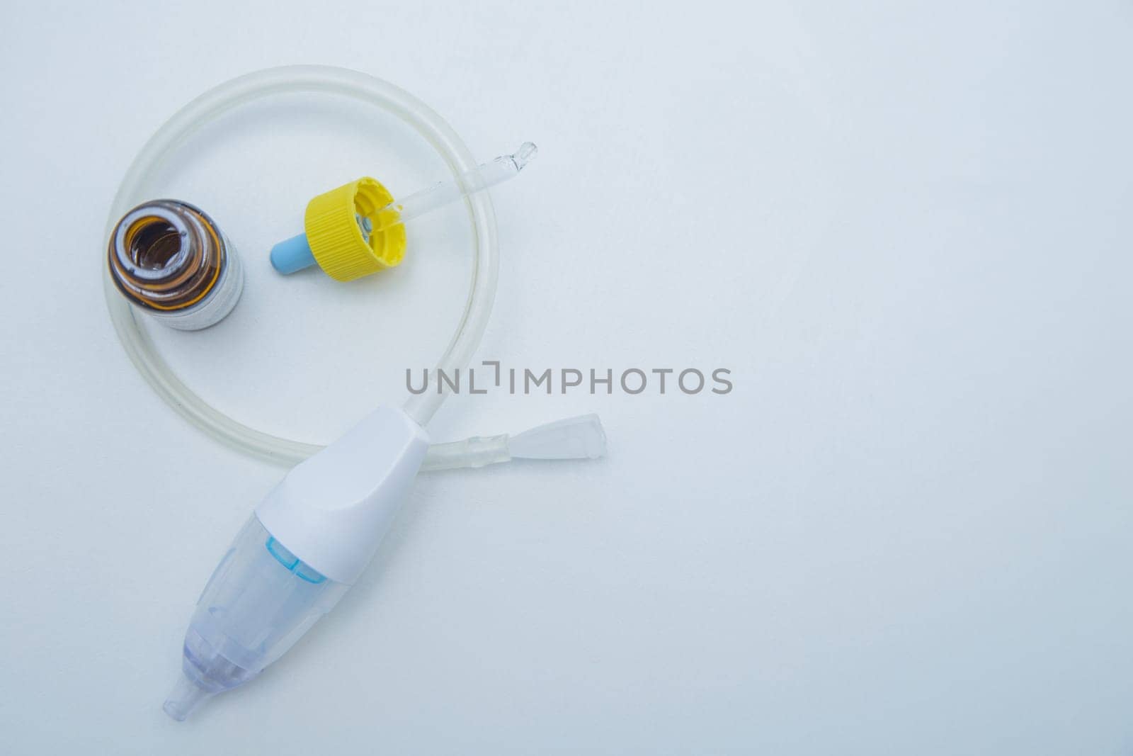 The children's aspirator lies rolled up in a ring on a white background, inside it are drops from a runny nose with a pipette. . High quality photo