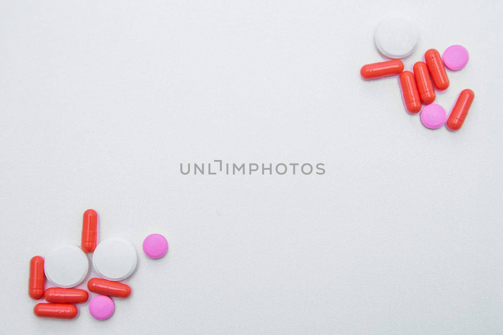 Tablets and capsules of white and pink color lie in opposite corners of the photo with space for text on a white background. High quality photo