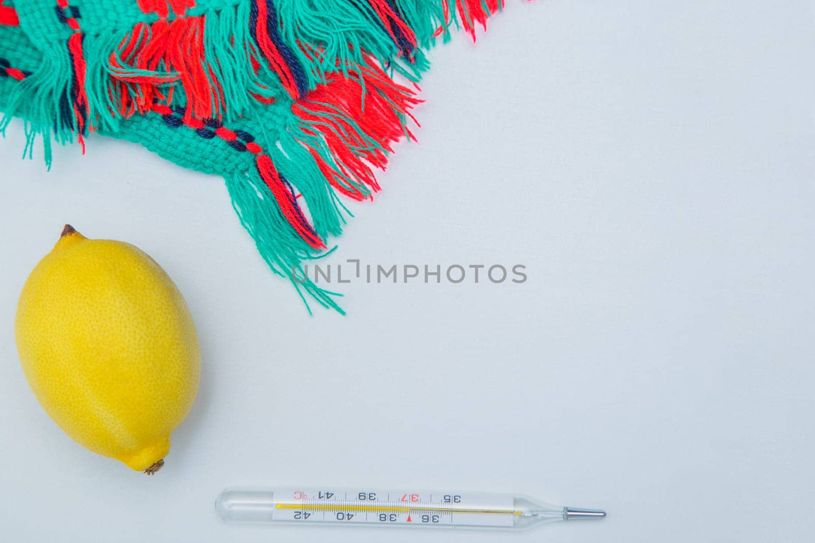 A warm winter scarf, thermometer, lemon lie on the side on a white background with a place for text. High quality photo