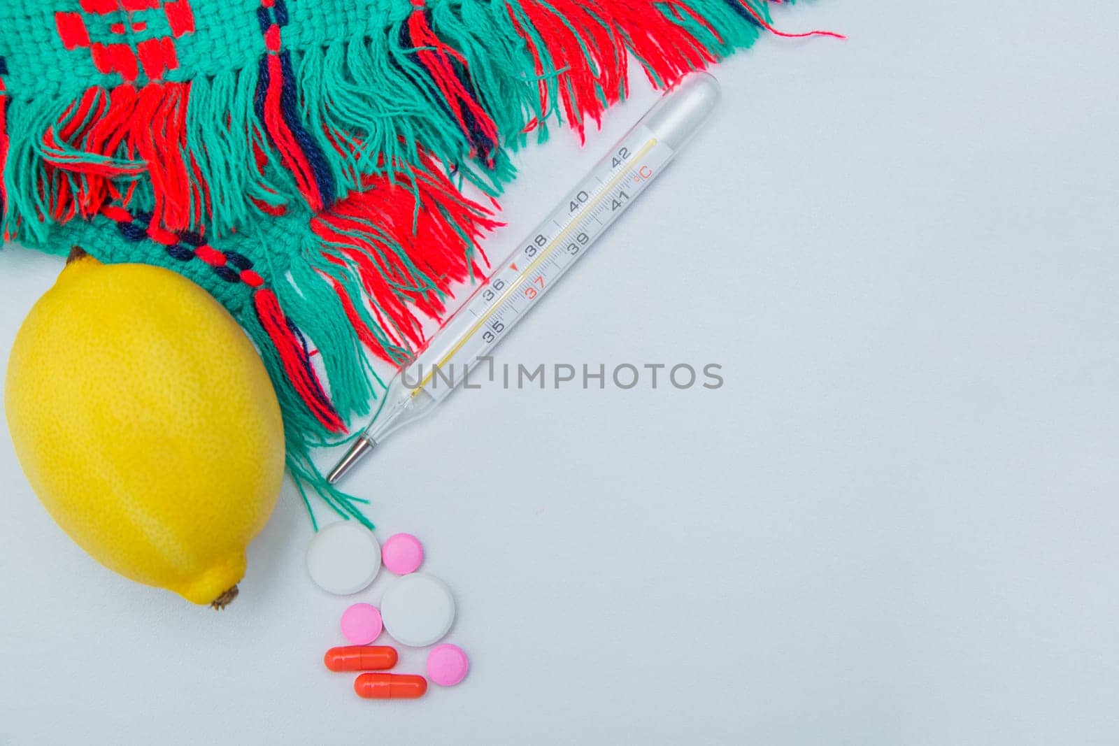 A warm winter scarf, thermometer, lemon and pills with capsules lie on the side on a white background with a place for text. High quality photo