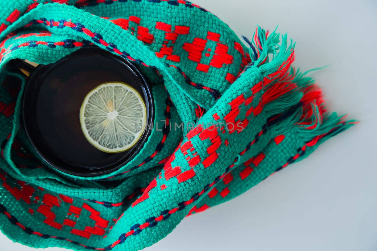 A cup of tea with lemon wrapped in a green and red scarf. . High quality photo
