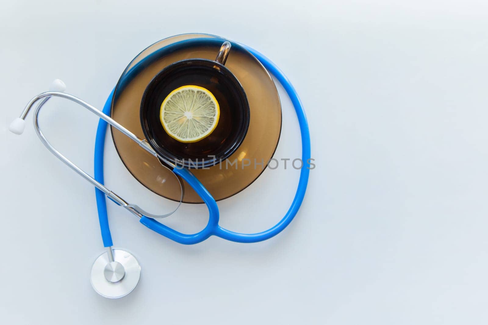 The blue stethoscope lies on a white background with a mug of tea on a saucer with a lemon in the middle. High quality photo
