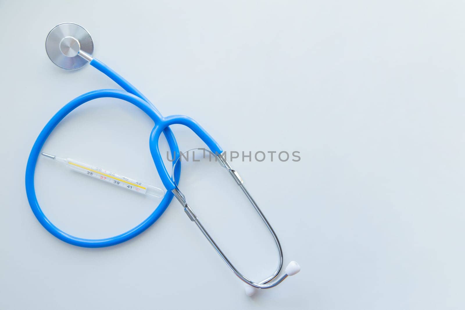 The blue stethoscope lies on a white background with a thermometer in the middle. . High quality photo