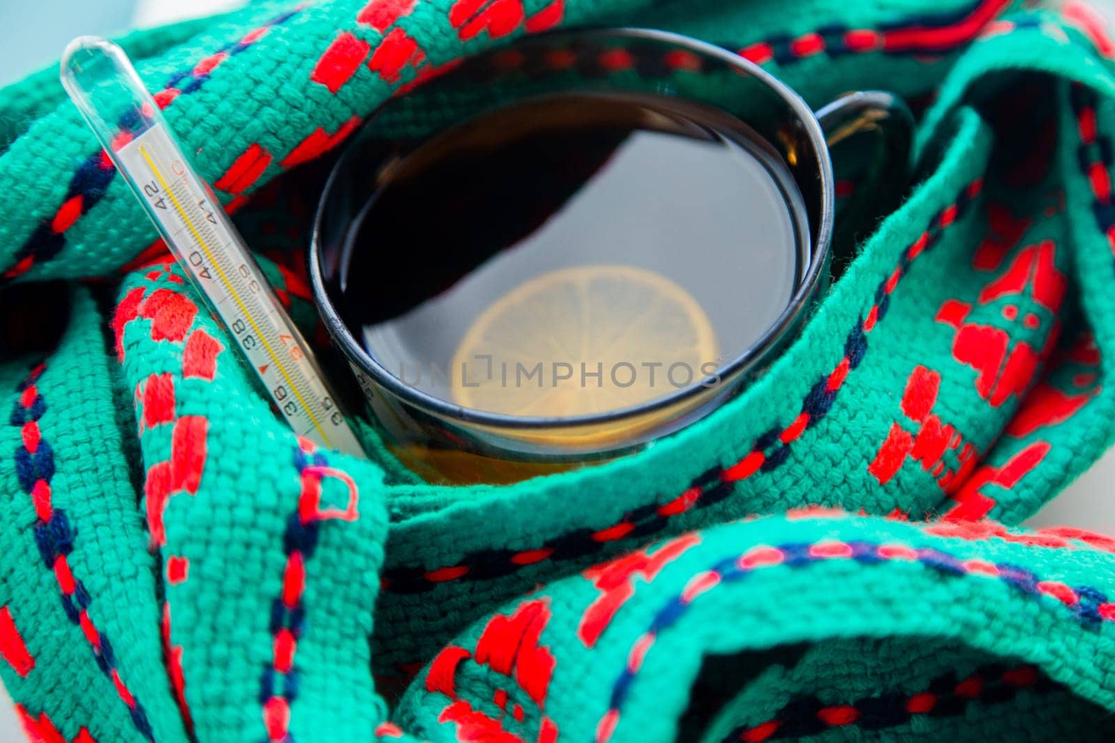 A cup of tea with lemon wrapped in a green and red scarf with a thermometer. High quality photo