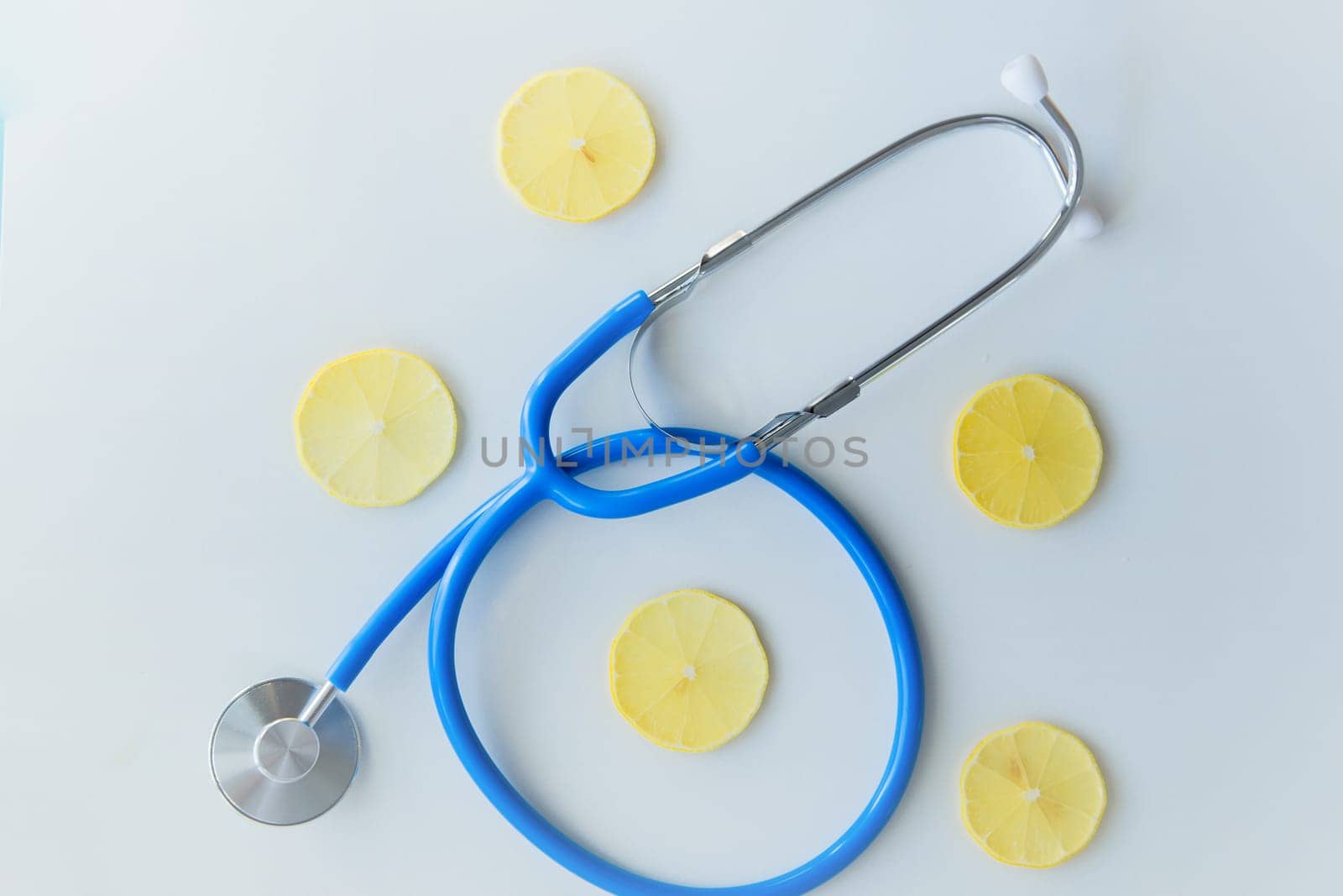 The blue stethoscope lies on a white background surrounded by lemon slices. High quality photo