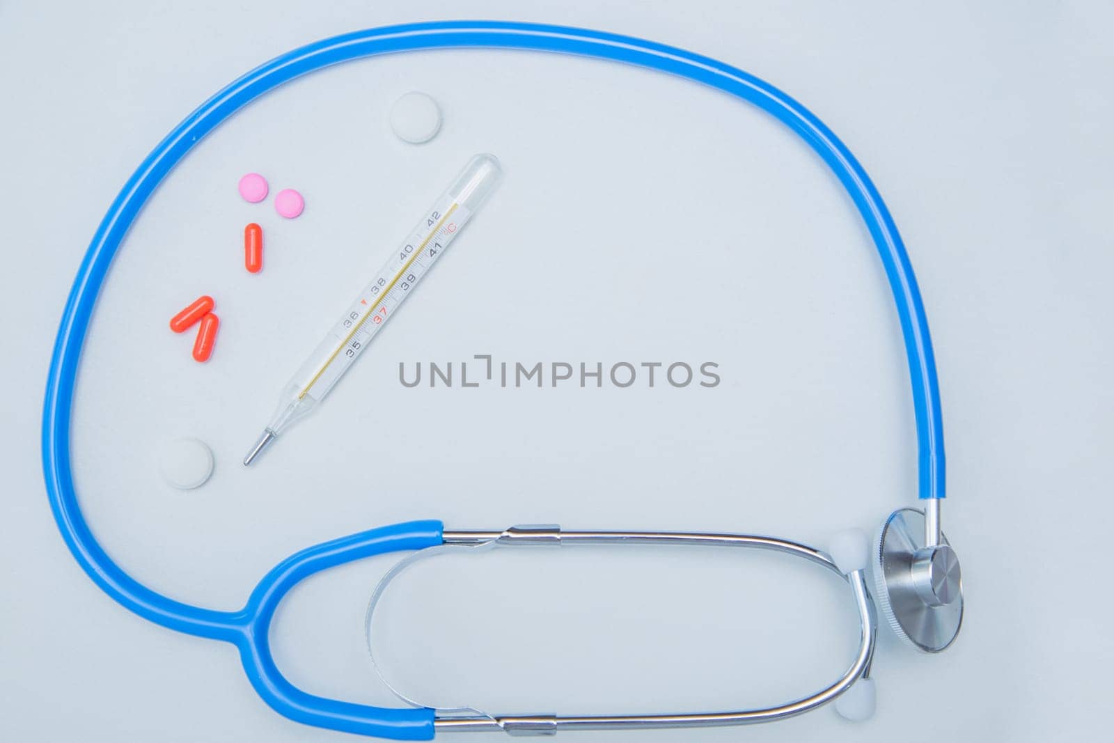 The stethoscope lies on a white background in a circle, inside it is a thermometer and a bunch of pills with a place for text are scattered. . High quality photo