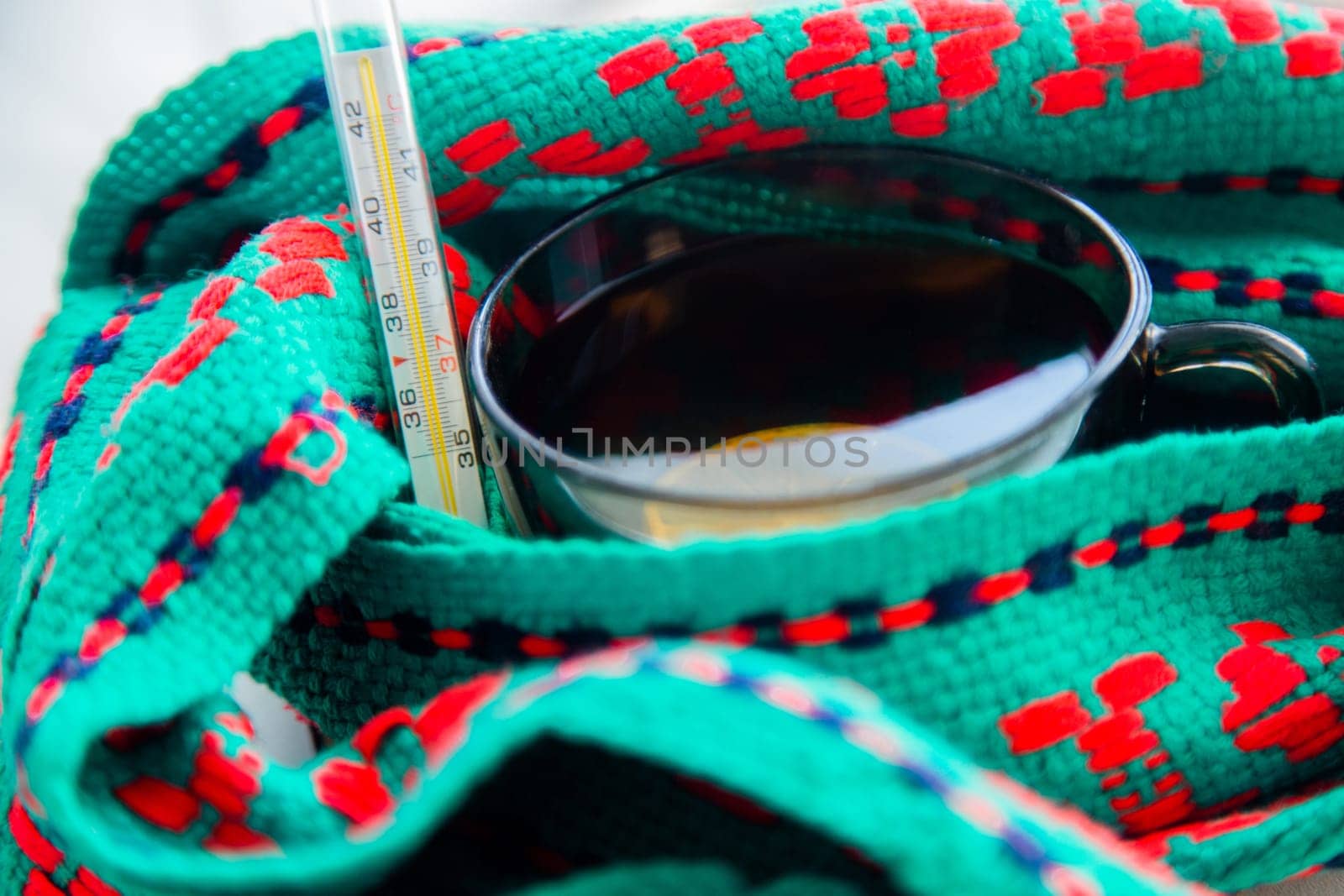 A cup of tea with lemon wrapped in a green and red scarf with a thermometer. High quality photo