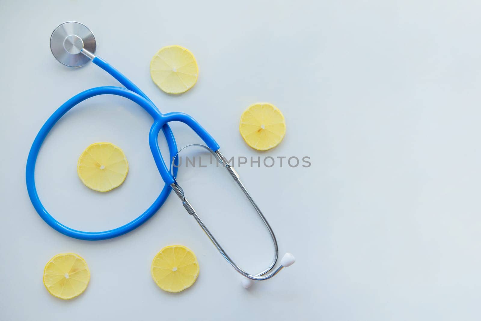 The blue stethoscope lies on a white background surrounded by lemon slices. High quality photo