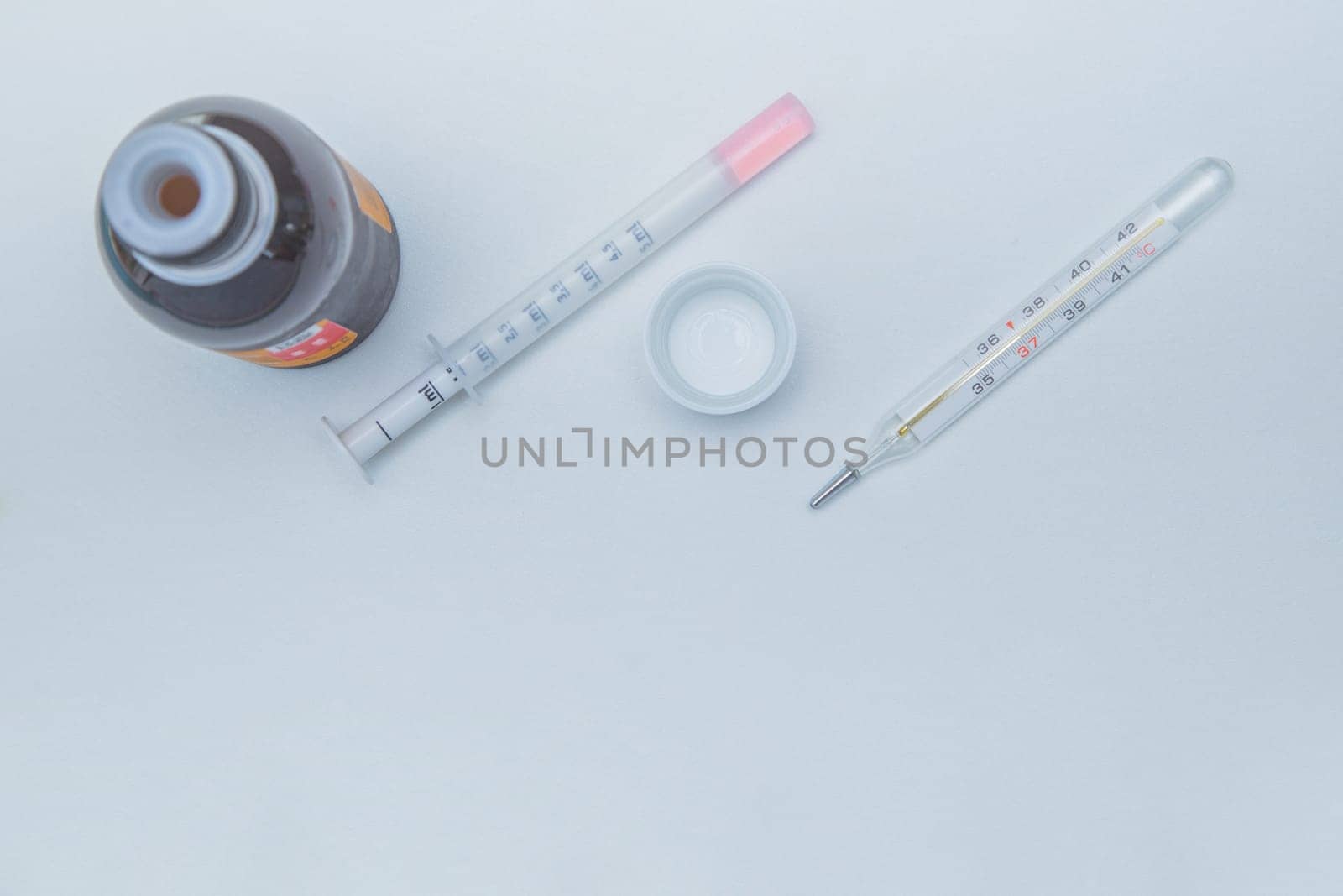 A medicine with a measuring syringe and a thermometer lies a white background. High quality photo