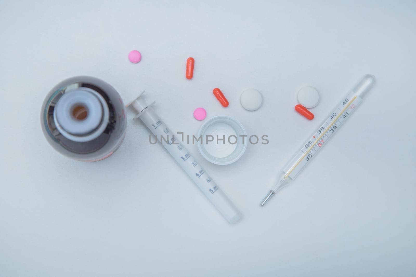 A medicine with a measuring syringe, tablets and capsules and a thermometer lies on the side against a white background. High quality photo