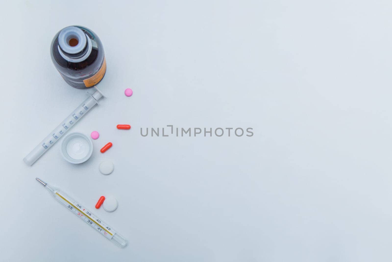A medicine with a measuring syringe, tablets and capsules and a thermometer lies on the side against a white background. High quality photo