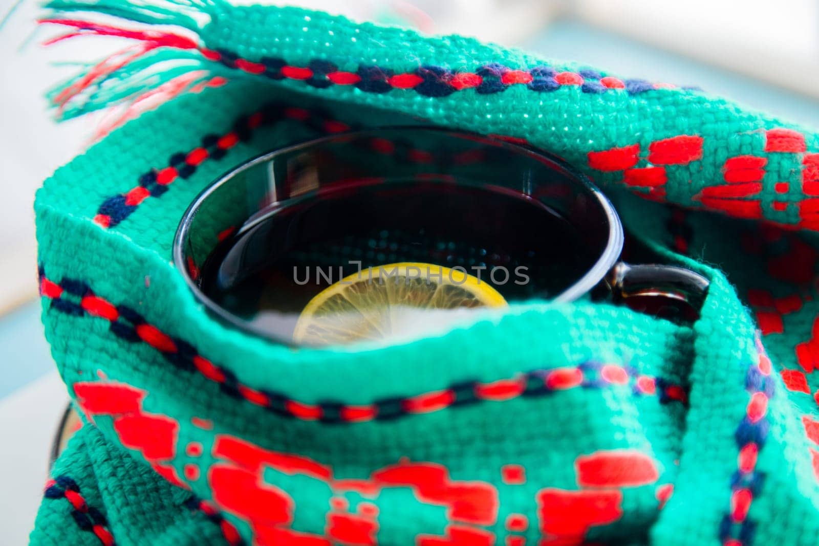 A cup of tea with lemon wrapped in a green and red scarf. . High quality photo