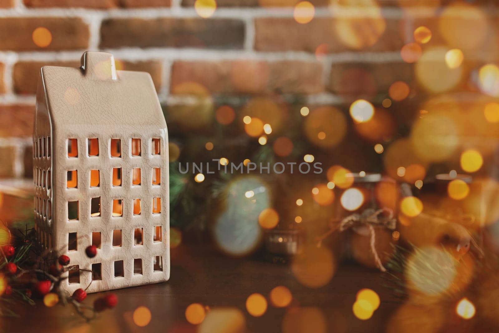 Christmas candle in form of house or home, symbol of family celebration, blurred background with Christmas fir tree festive decorations, lights, garlands. Festive mood at home. High quality photo