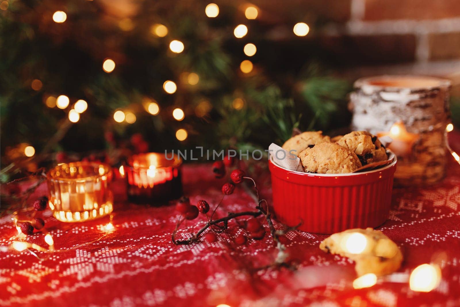 Red festive bowl full with tasty Christmas chocolate cookies, blurred background with Christmas fir tree decorations, lights, garlands and candles. Festive mood at home. High quality photo