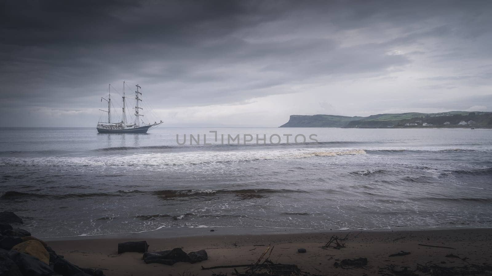 Dark, dramatic storm sky rolling over anchored tall ship near Northern Ireland coast with Fair Head in far distance, Ballycastle
