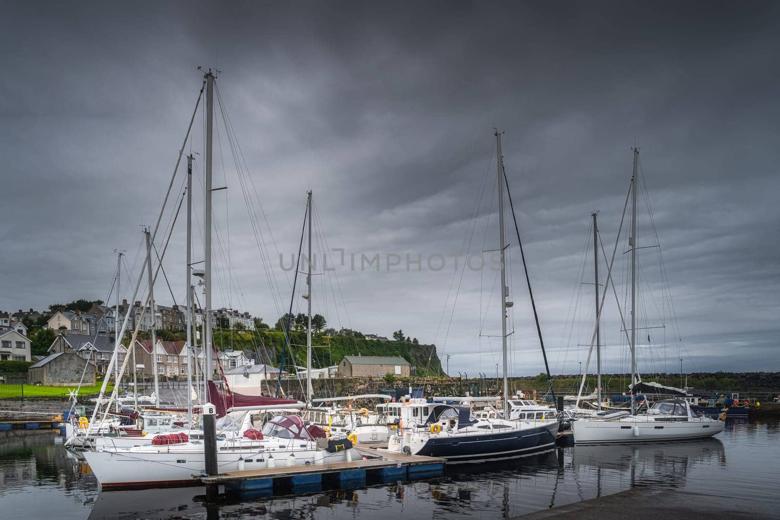 Yachts and sailboats moored in small, beautiful marina in Ballycastle town with dark storm clouds, Antrim, Northern Ireland