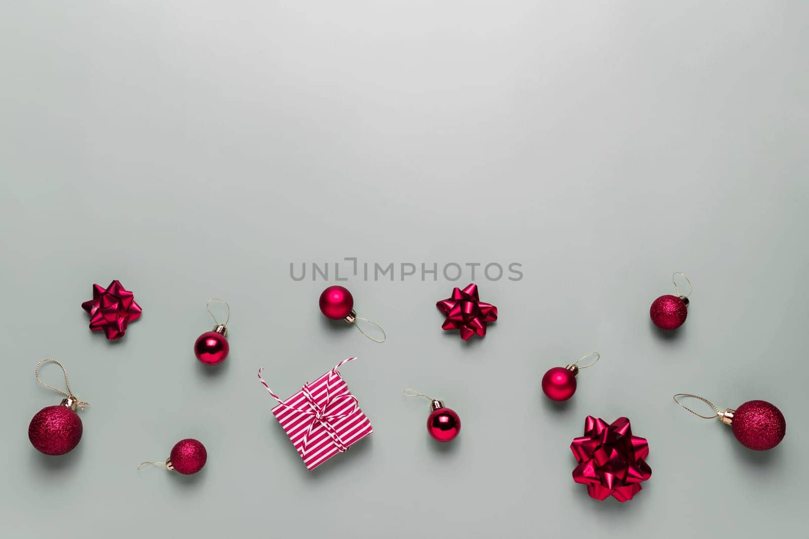 Gray background with pink Christmas gift box present, small red Christmas balls or sphere toys, ribbon bows for fir tree, other decorations. Christmas sales, shopping or greeting card or invitation
