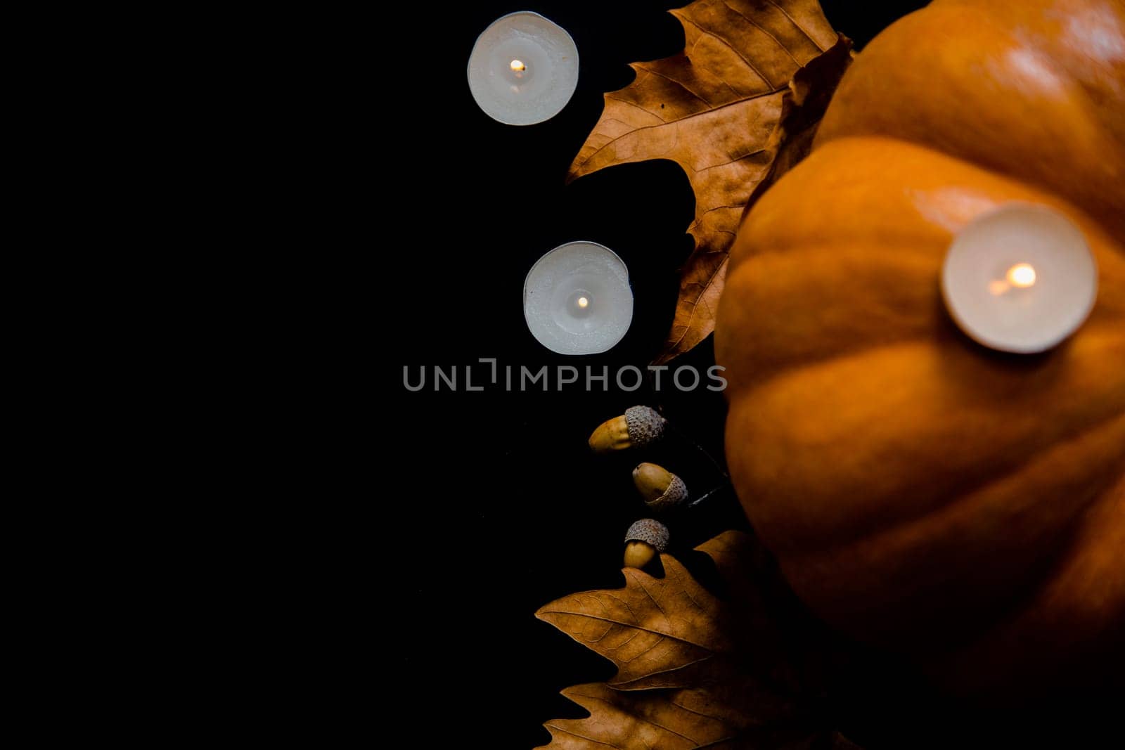 An orange pumpkin with leaves, acorns and candles on a black background. High quality photo
