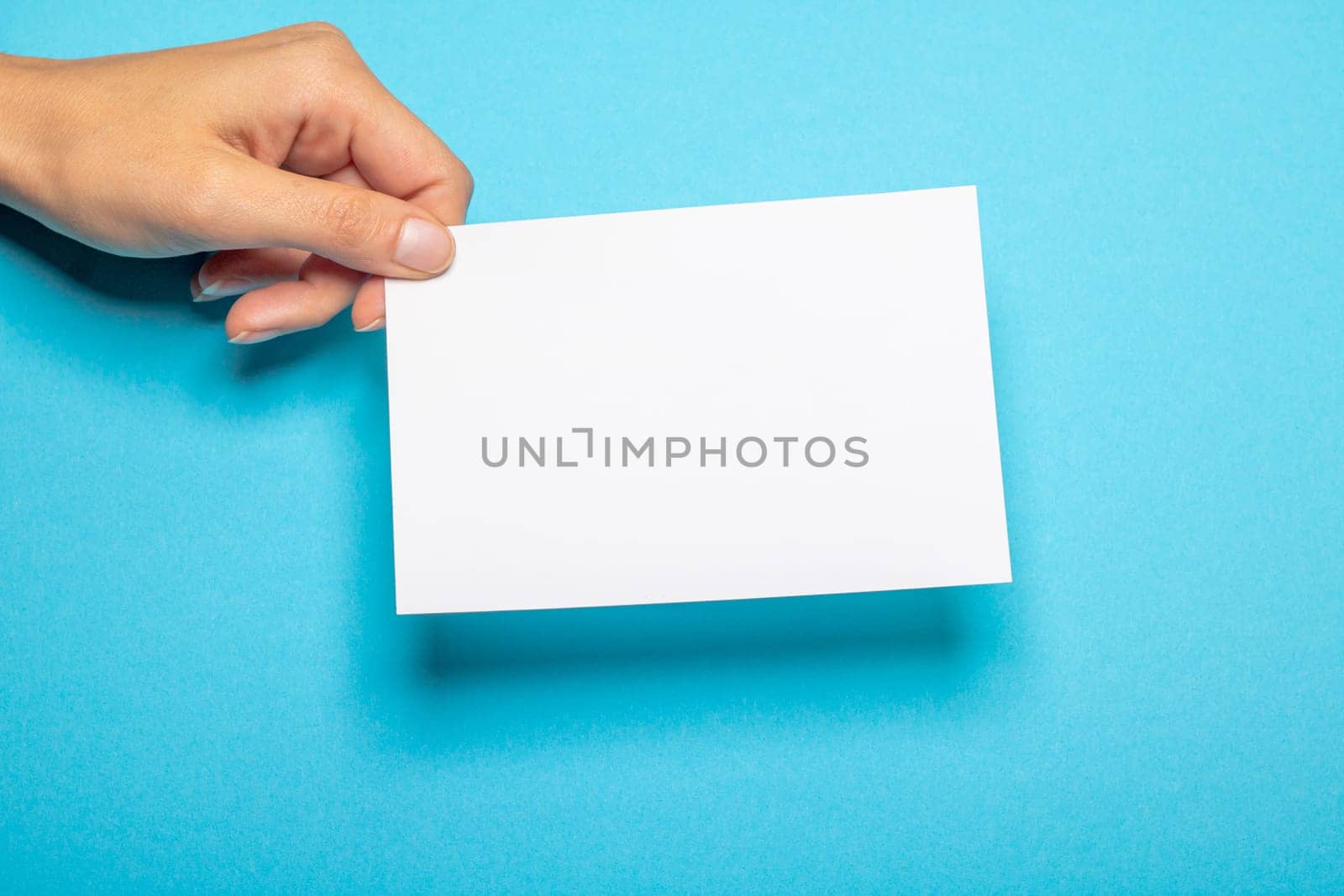 female hand holds a blank piece of paper with copy space in front of a light blue background cardboard