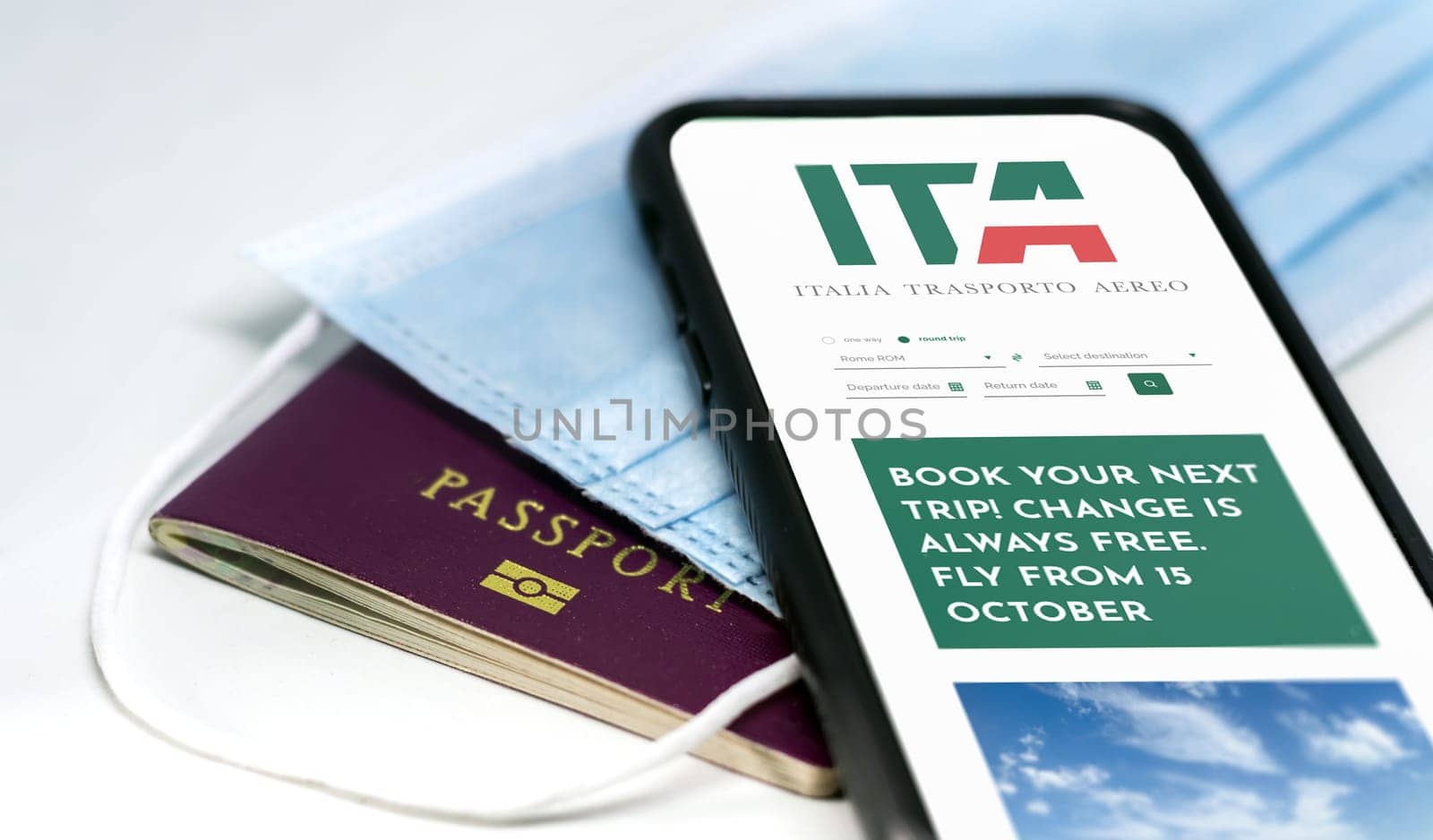 Rome, Italy, October 2021: phone with the ITA app on the screen over a surgical mask and a passport. ITA is the new Italian flag carrier starting from 15 October 2021. Travel in pandemic times