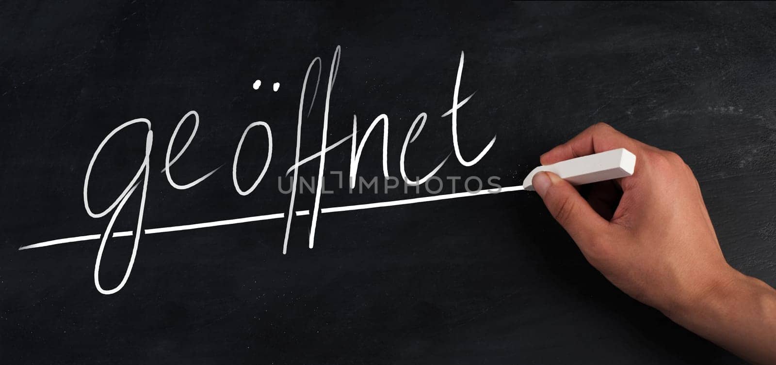 The word open is standing in german language on a chalkboard, handwritten