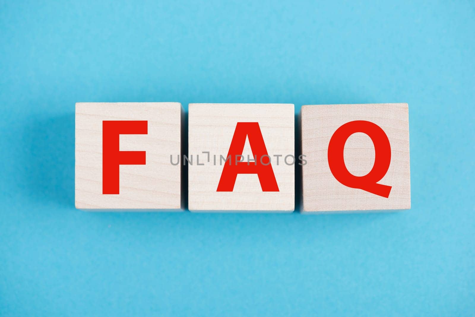 The letters FAQ are standing on wooden cubes, blue colored background, frequently asked questions