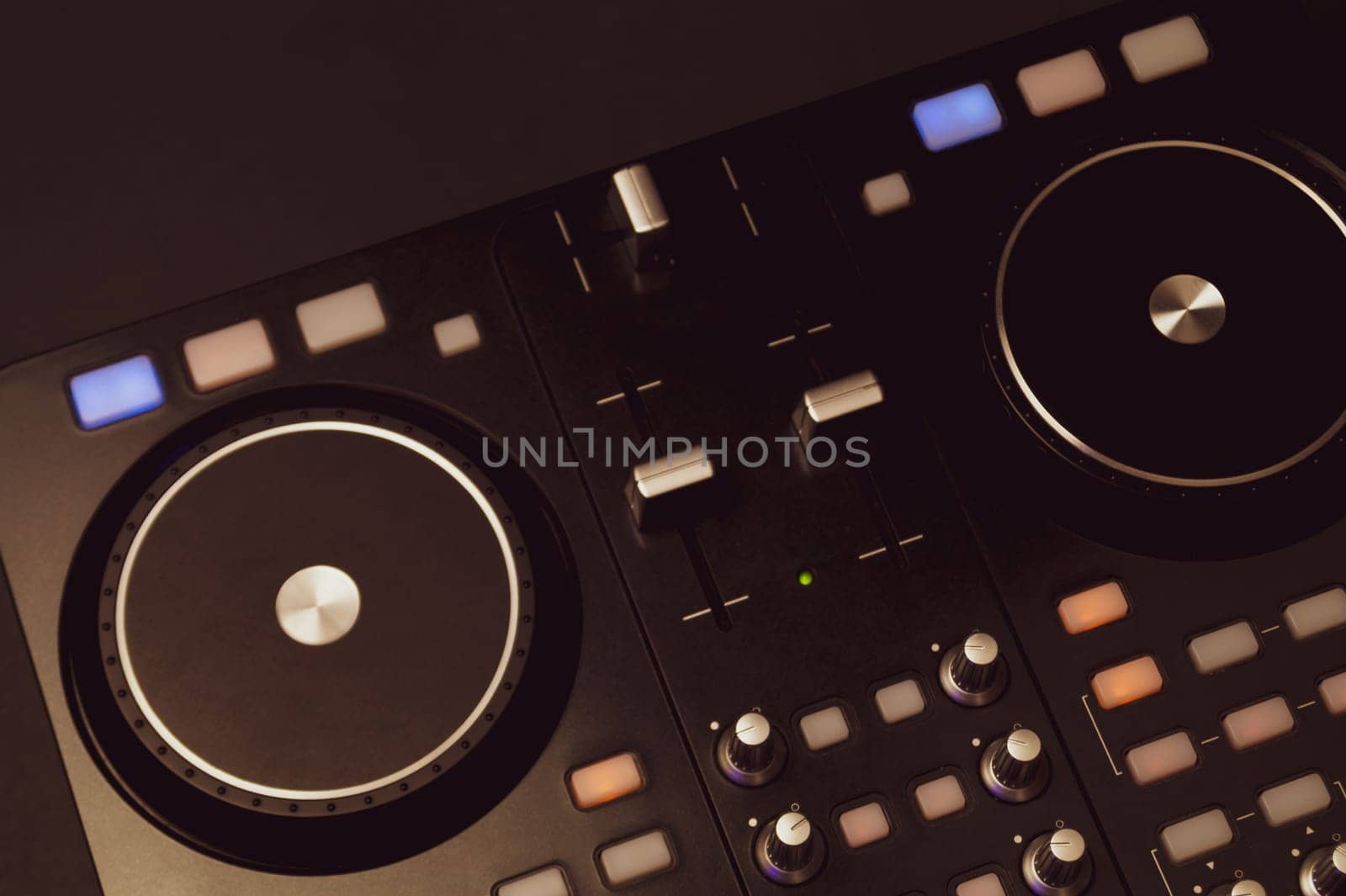 Dj sound mixer controller with knobs and sliders close up. audio mixing deck with turntables at dark with illuminated controls