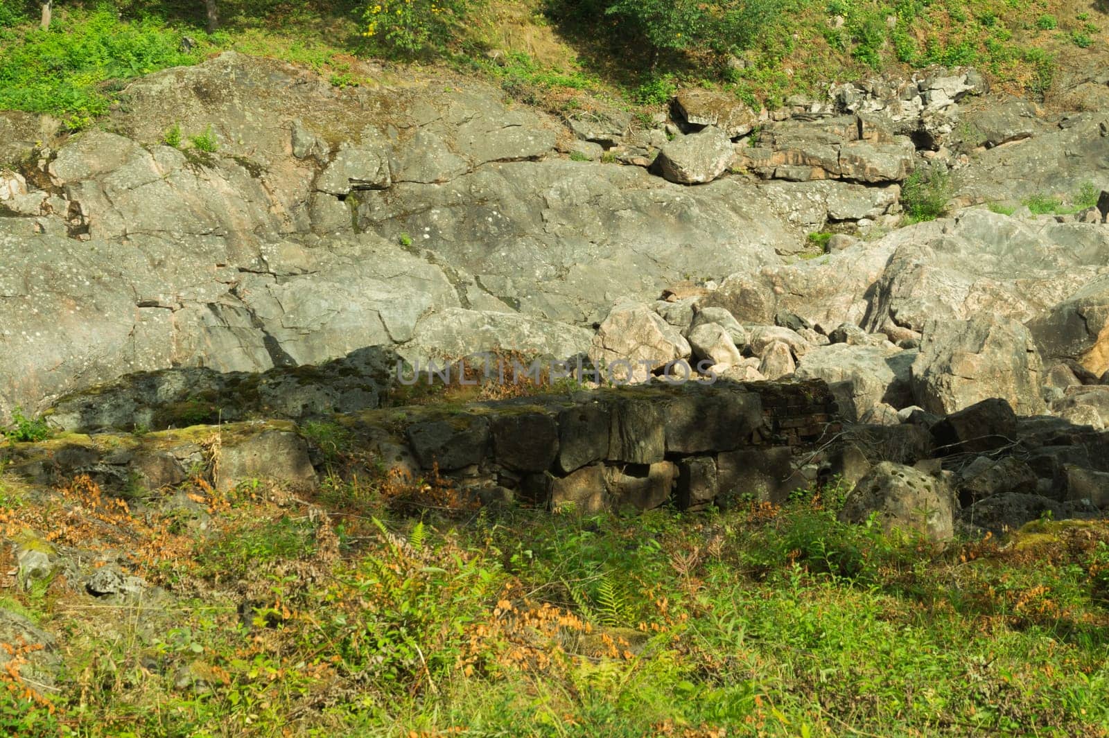 Rock of layered stone overgrown with grass and moss. texture of stone rocks. stone background