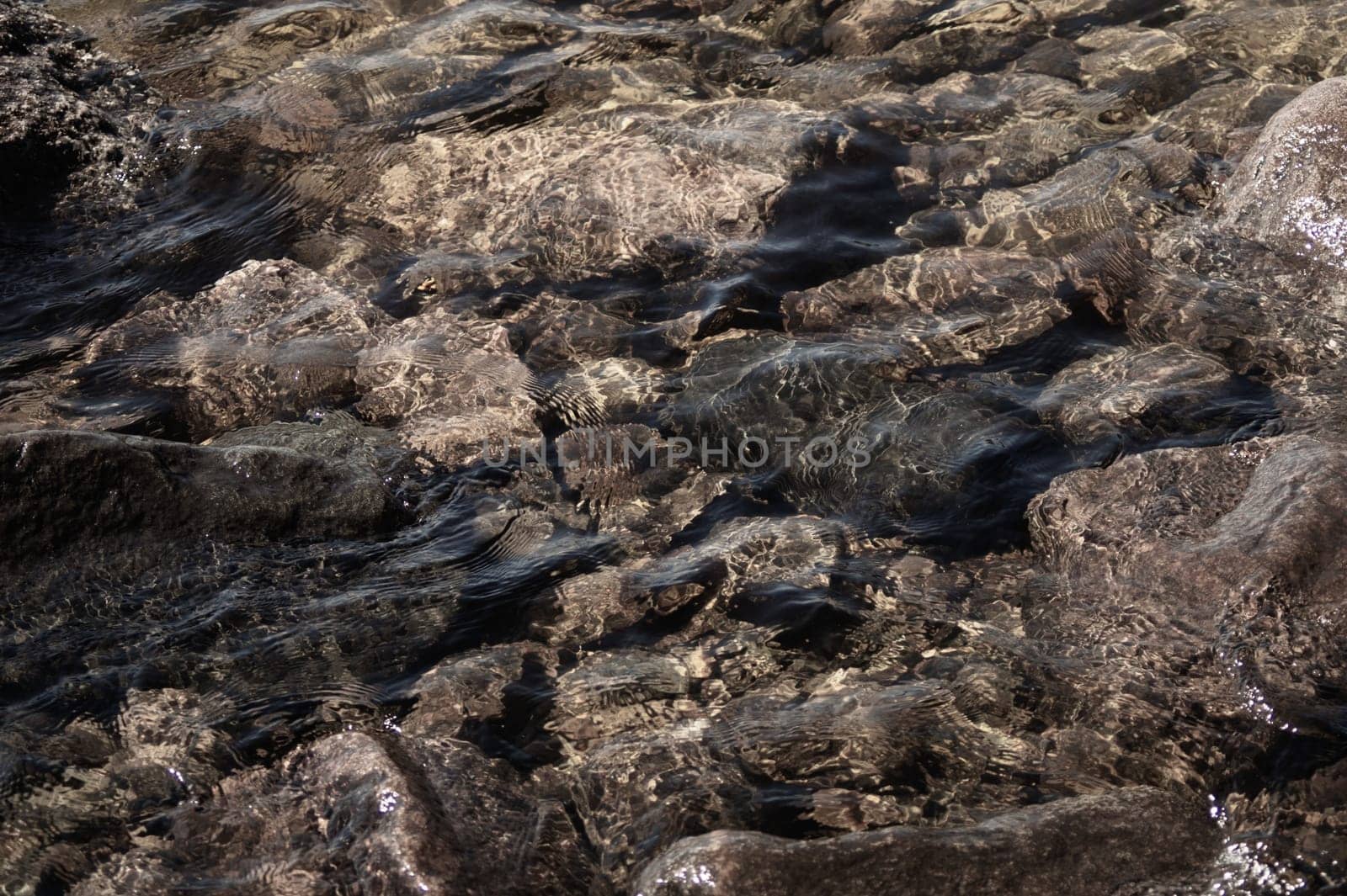 Shiny transparent water. clear water with pebbles and stone on the bottom. shining reflections of sun rays and ripples on the water surface