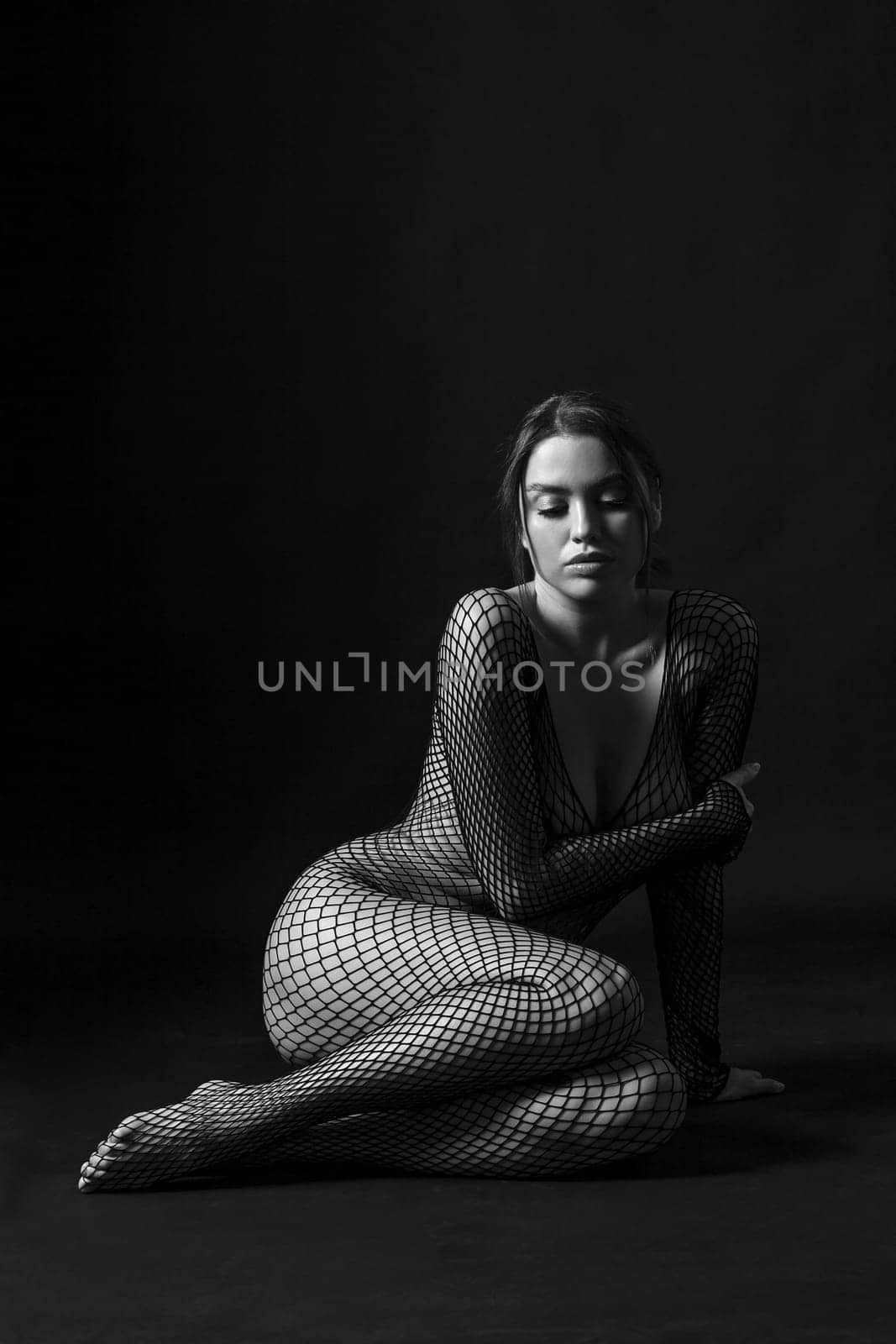 Sexy woman sitting and wearing full body fishnet stockings, done in black and white.