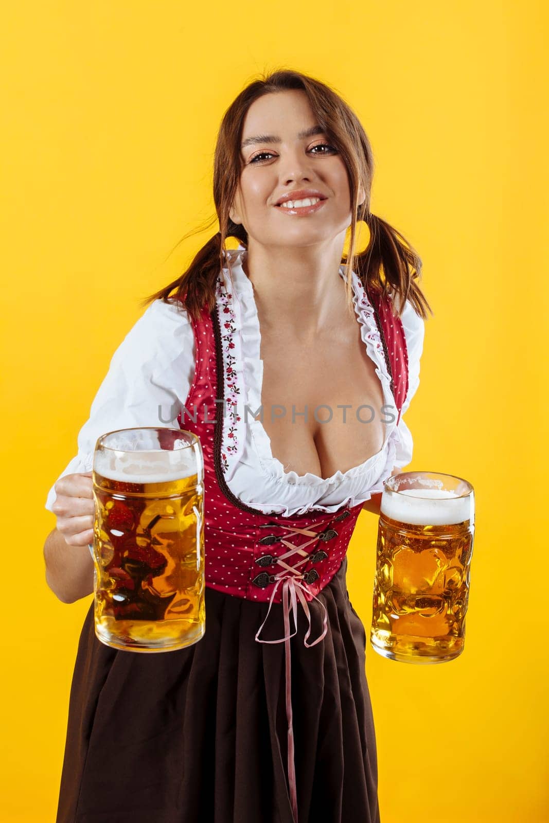 Beautiful Oktoberfest server wearing traditional dirndl and holding two mass beer steins.
