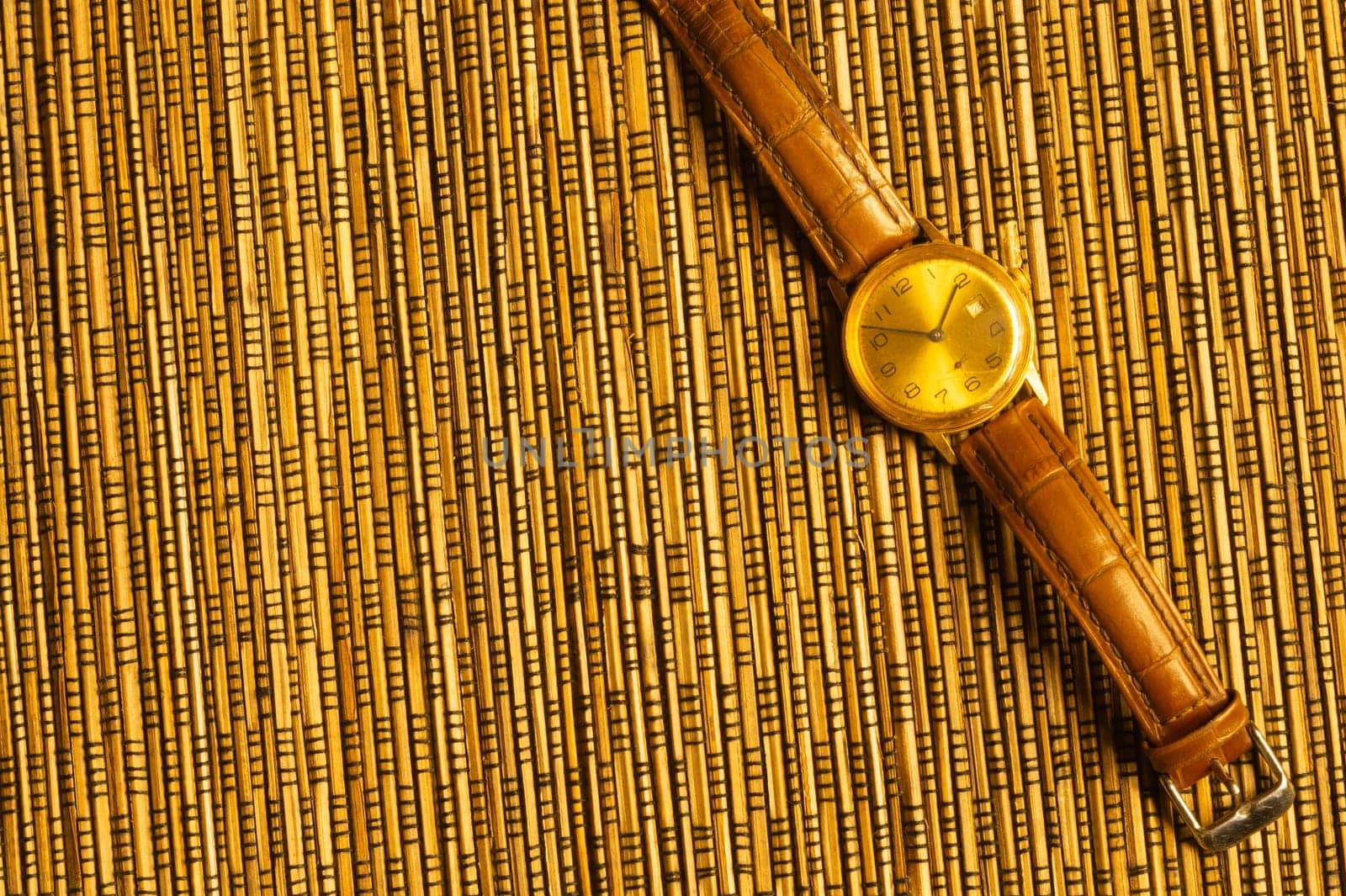Vintage golden wristwatch with leather strap on the bamboo background. copy space