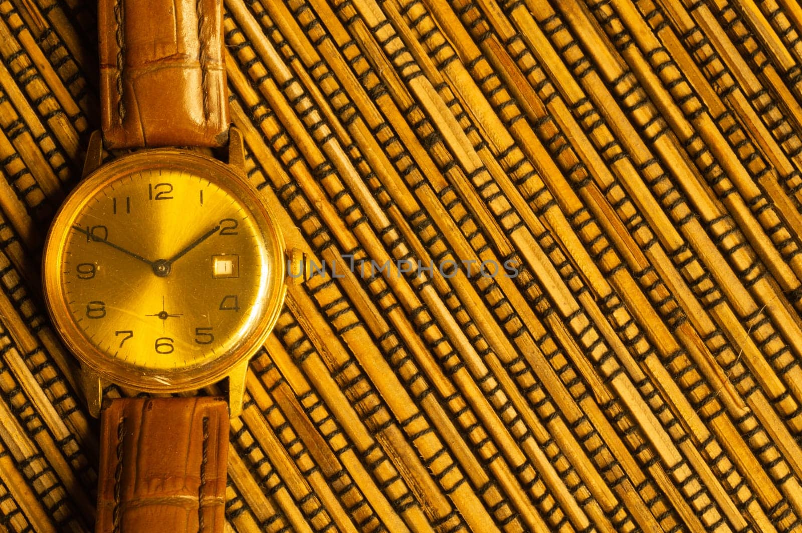 Vintage golden wristwatch with leather strap on the bamboo background. copy space
