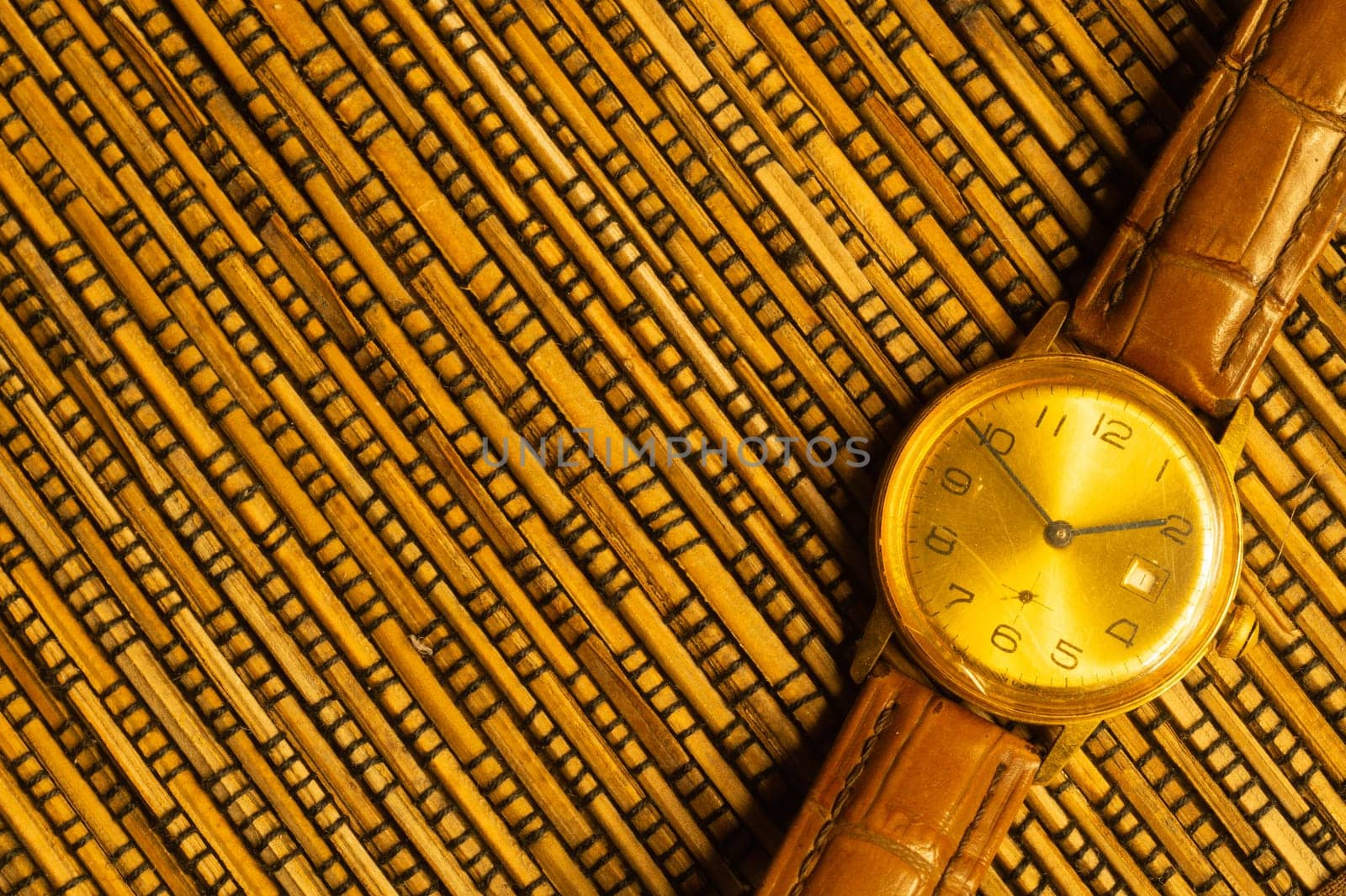 Vintage golden wristwatch with leather strap on the bamboo background. copy space