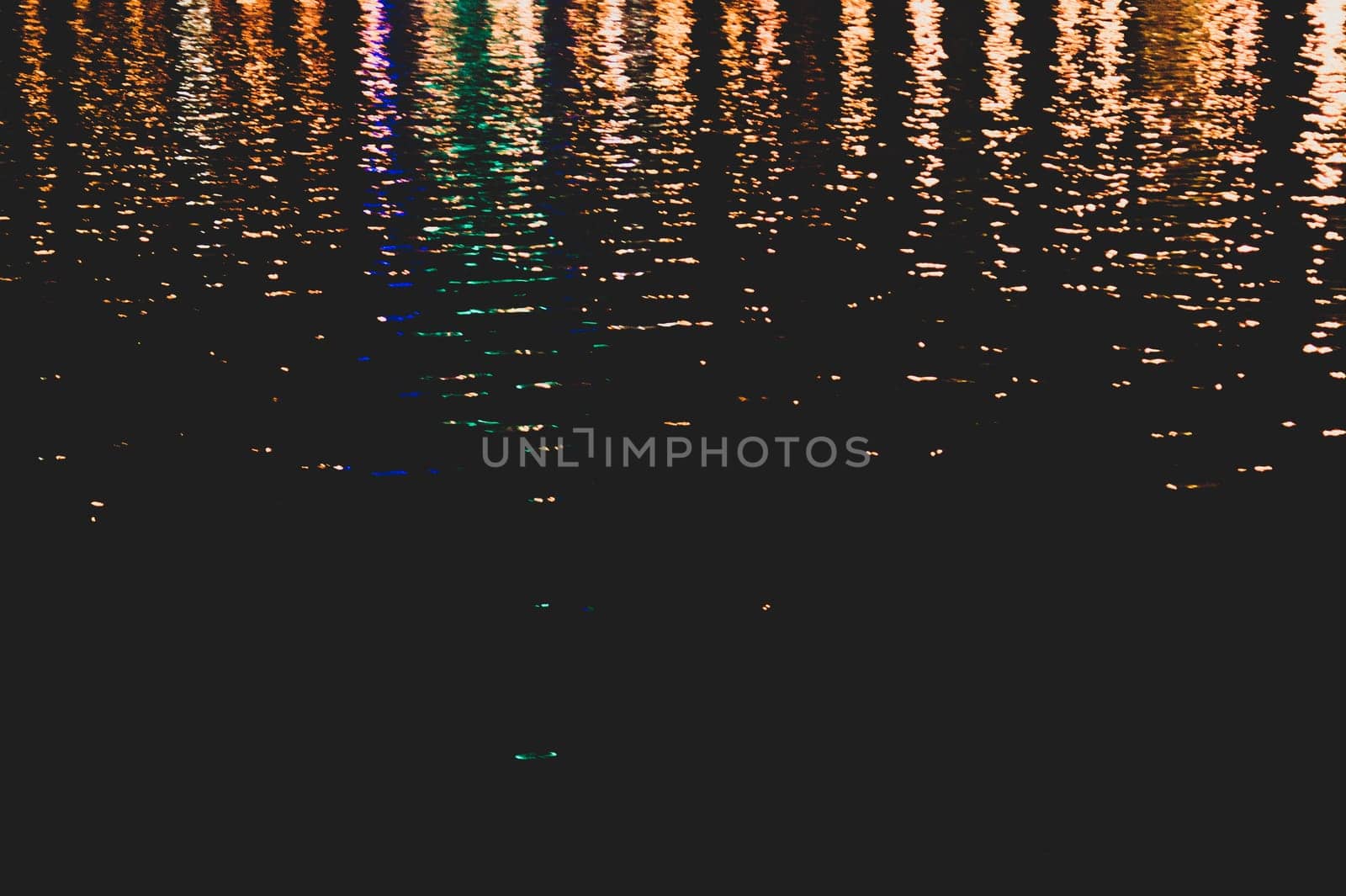 Blurred colorful lights reflect on water surface with ripples in the dark night. abstract background