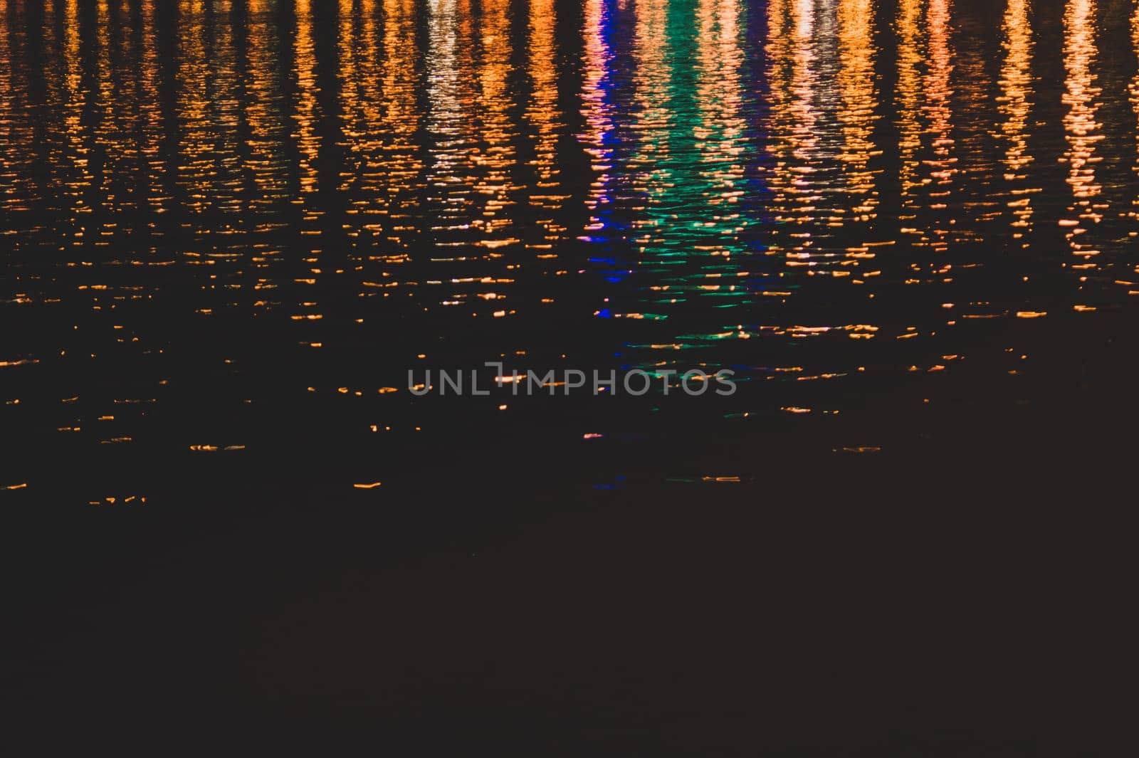 Blurred colorful lights reflect on water surface with ripples in the dark night. abstract background