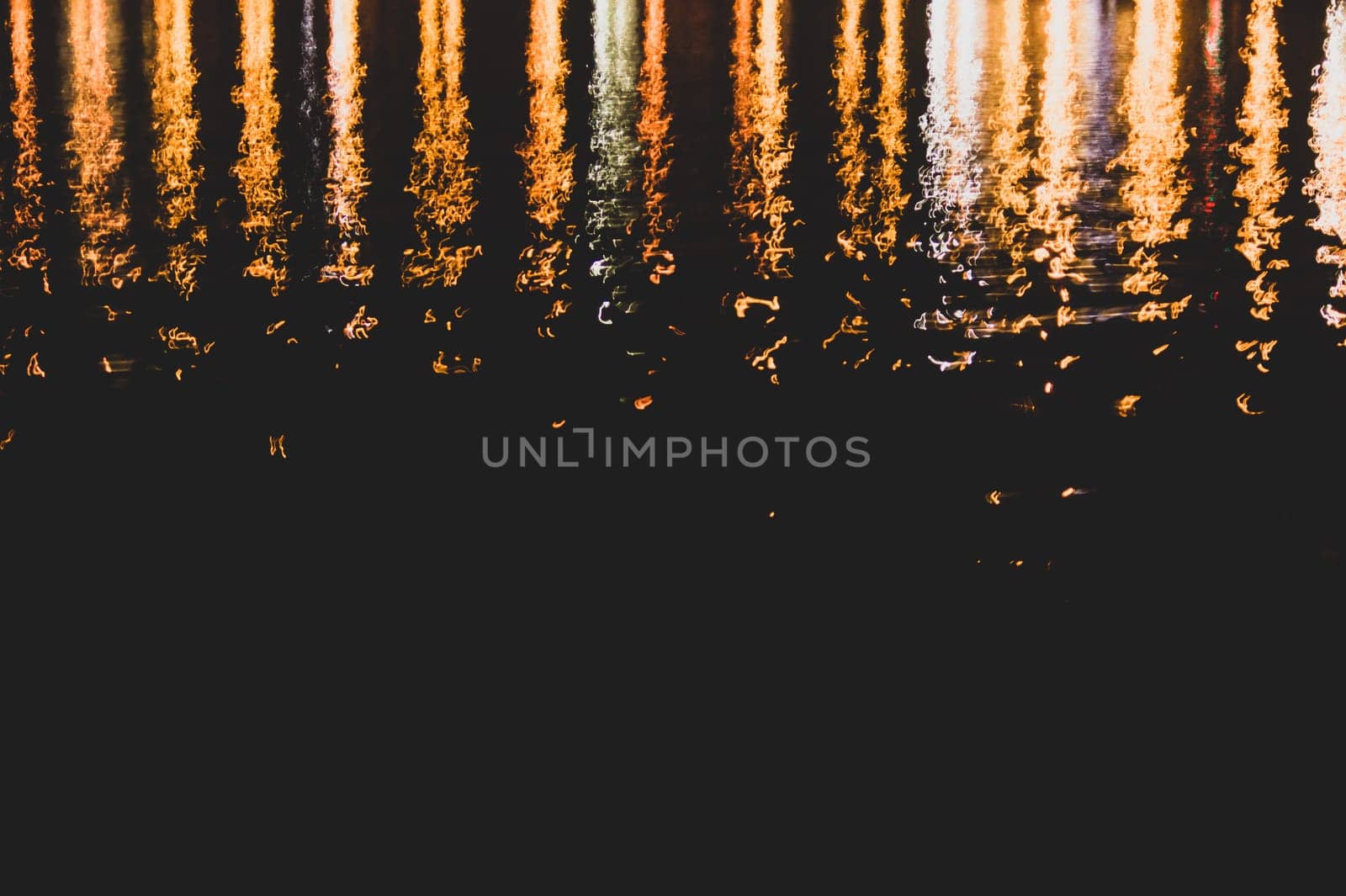Blurred colorful lights reflect on water surface with ripples in the dark night. abstract background