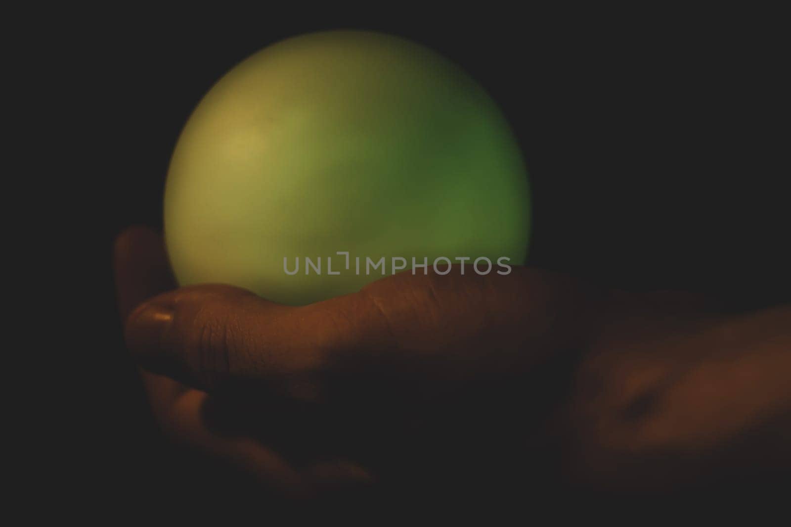 Hand holds a luminous sphere in the dark