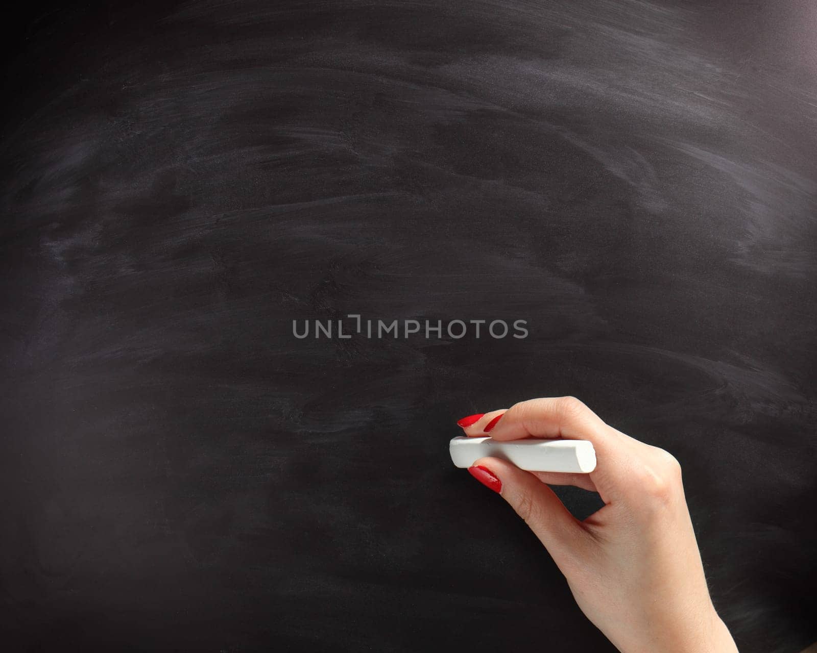 Close up Woman Hand with Nail Polish About to Write on Empty Black Chalkboard, Emphasizing Copy Space.