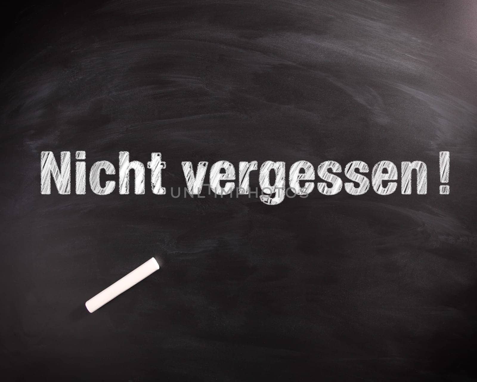 Conceptual Nicht Vergessen or Do not Forget Phrase in White on Black Chalkboard with Chalk on Top.