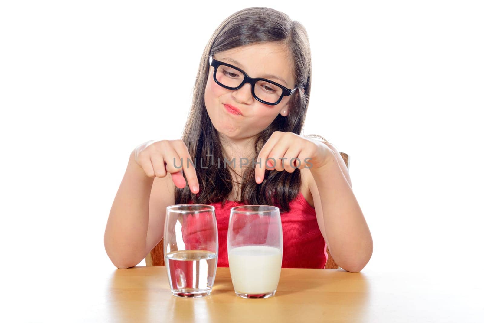 a little girl has a choice between a glass of water and a glass of milk