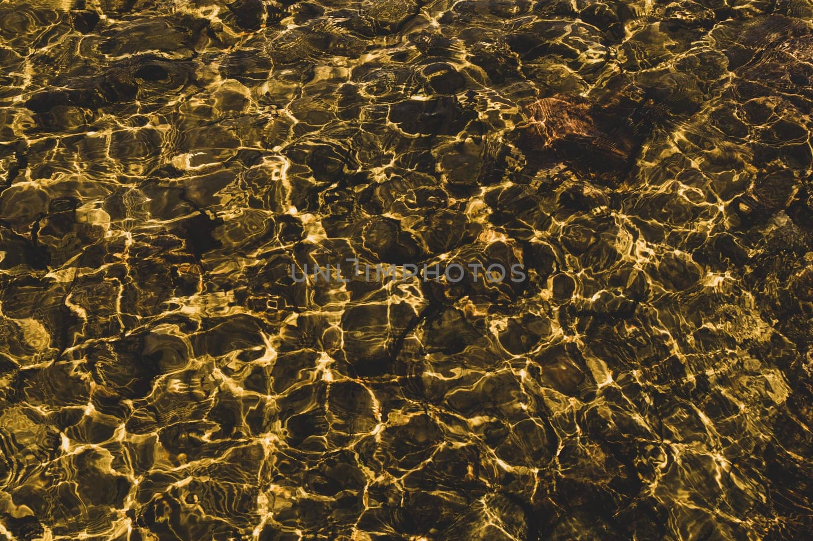 Shiny transparent water. clear water with pebbles and stone on the bottom. shining reflections of sun rays and ripples on the water surface