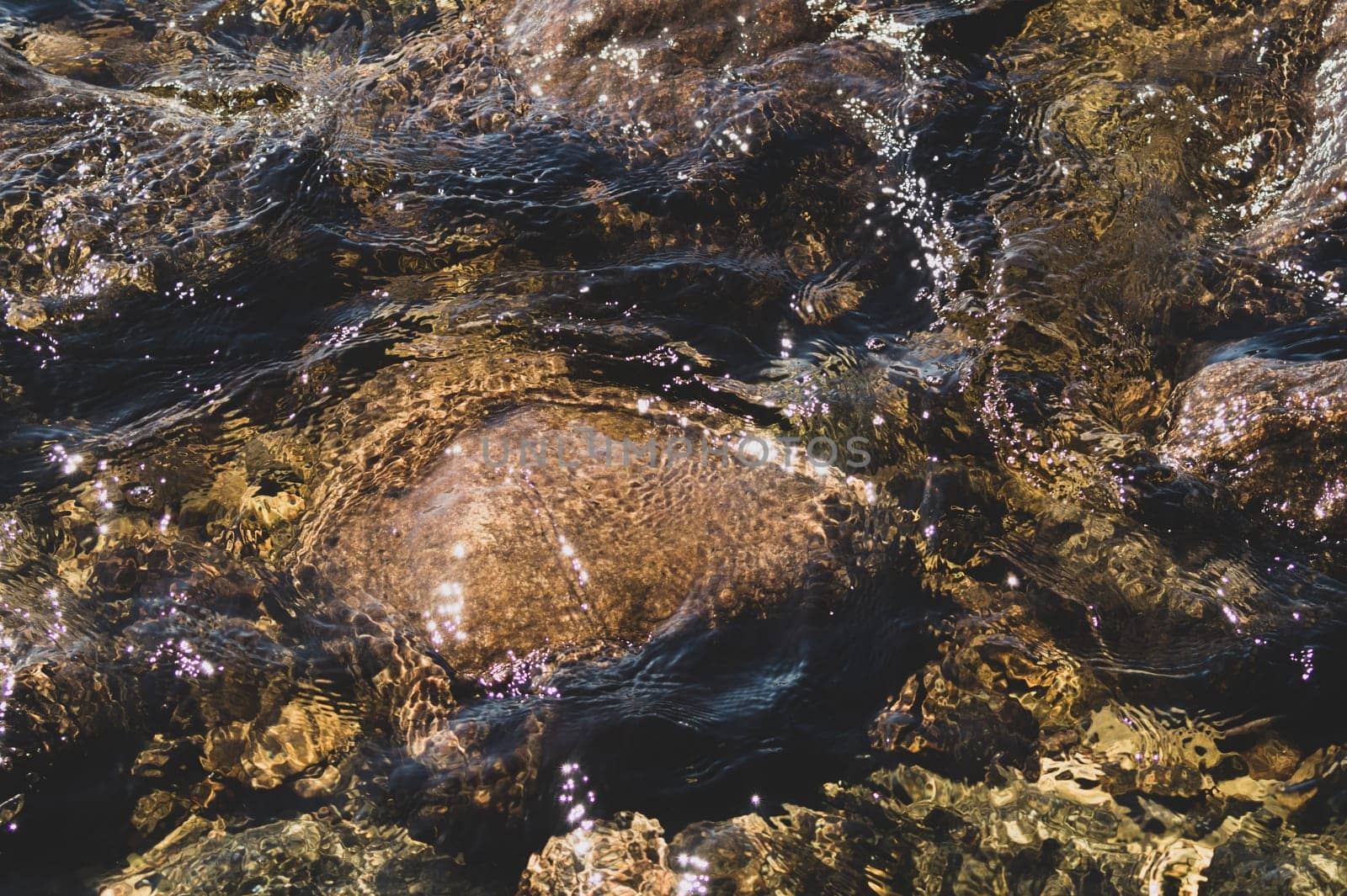 Shiny transparent water. clear water with pebbles and stone on the bottom. shining reflections of sun rays and ripples on the water surface