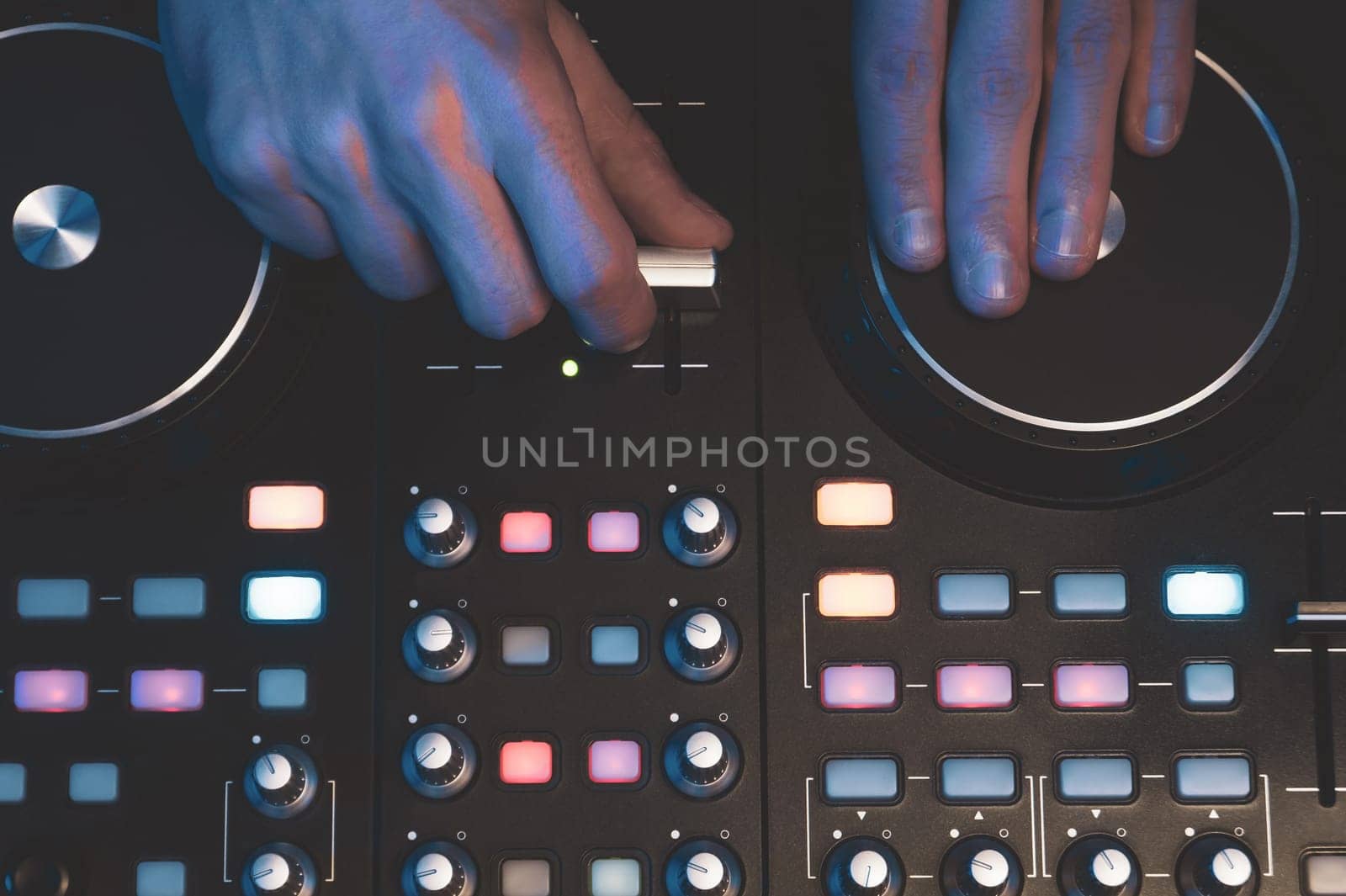 DJ plays music. sound mixer controller with knobs and sliders close up. hands on the mixing deck with turntables at dark with illuminated controls