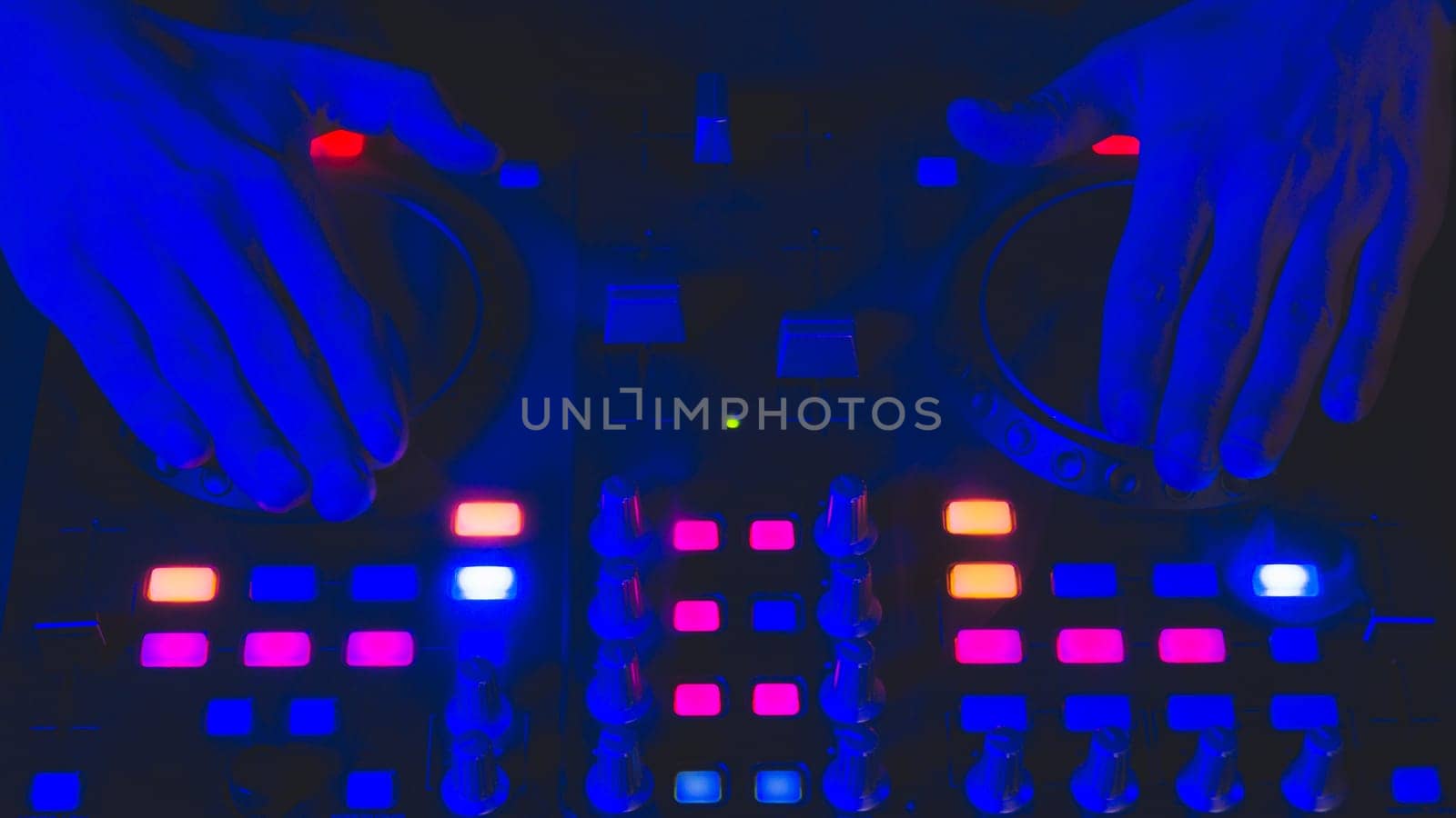 DJ plays music. sound mixer controller with knobs and sliders close up. hands on the mixing deck with turntables at dark with illuminated controls